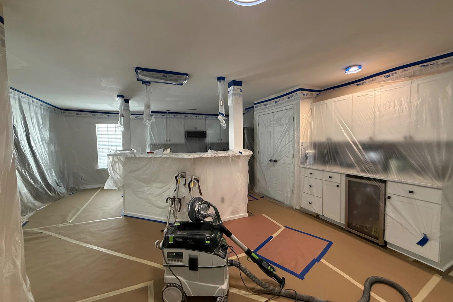 Kitchen and living area fully protected with floor covering, plastic containment, and HEPA dust extraction during ceiling work